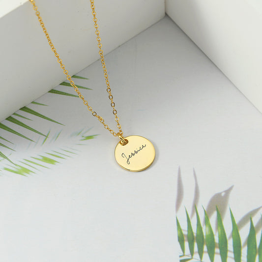 Gold disc necklace pendant displayed on a white background with palm leaves in the background.