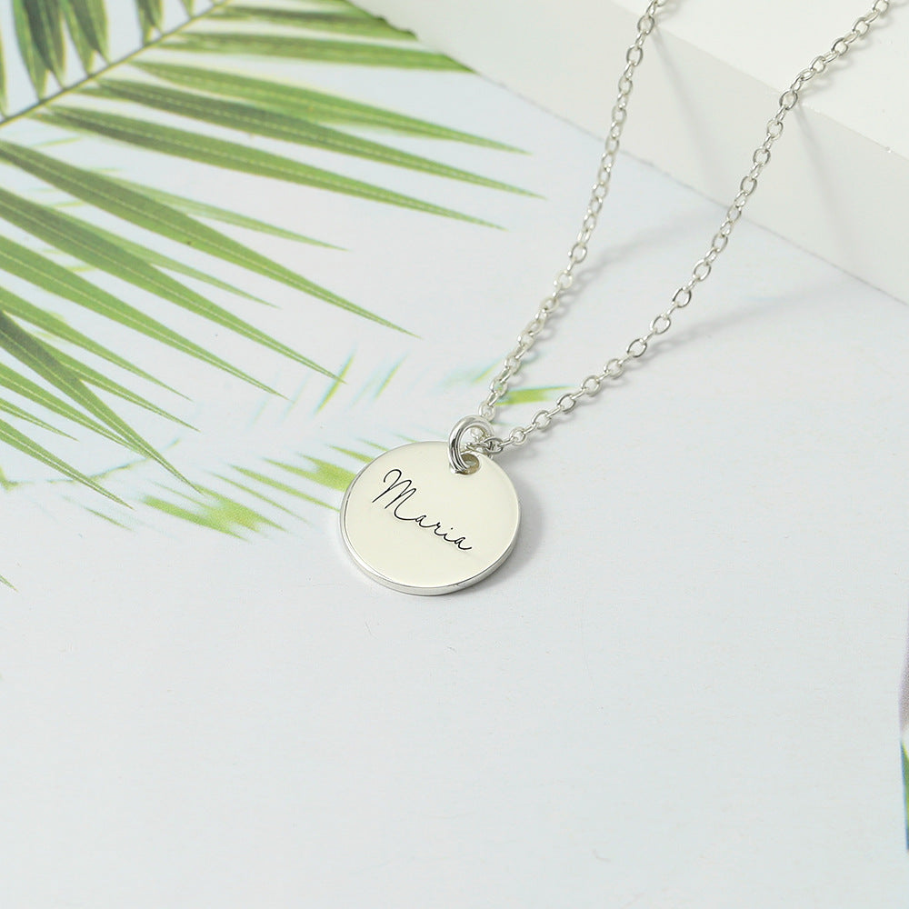 Silver disc necklace pendant displayed on a white background with palm leaves in the background.