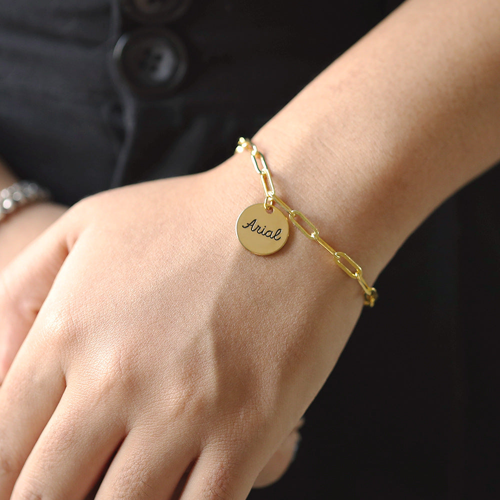 A gold-coloured bracelet with a round disc charm personalised with the name 'Arial'.