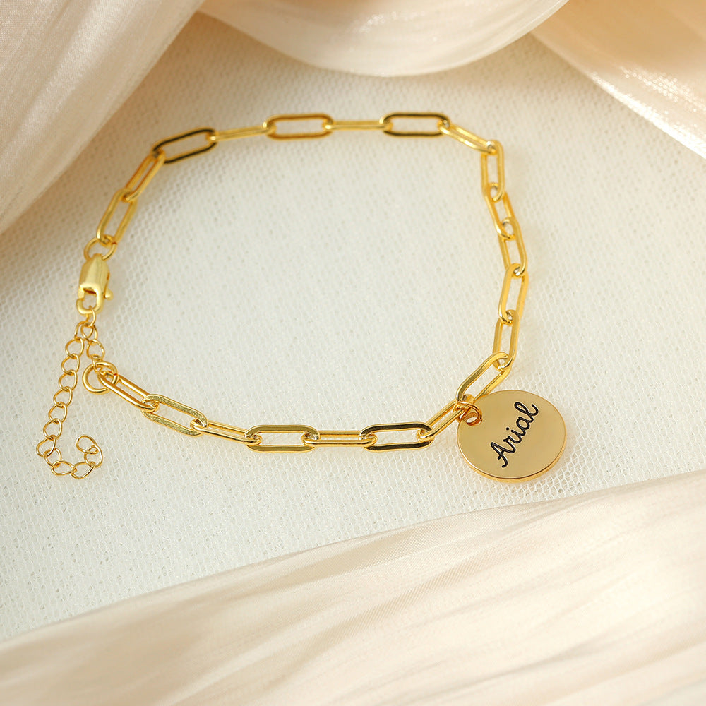 A gold-coloured bracelet with a round disc charm personalised with the name 'Arial'.