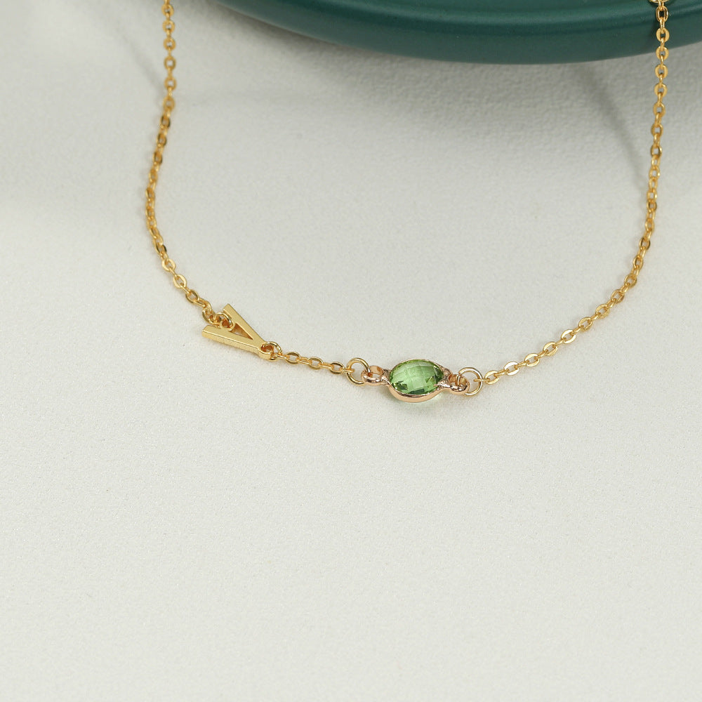 A gold-coloured bracelet with an emerald pendant and a customisable initial charm.