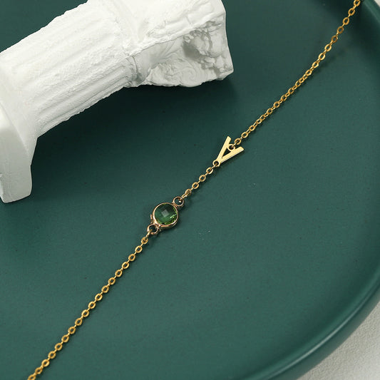 A gold-coloured bracelet with an emerald pendant and a customisable initial charm.