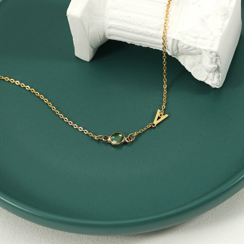 A gold-coloured bracelet with an emerald pendant and a customisable initial charm.