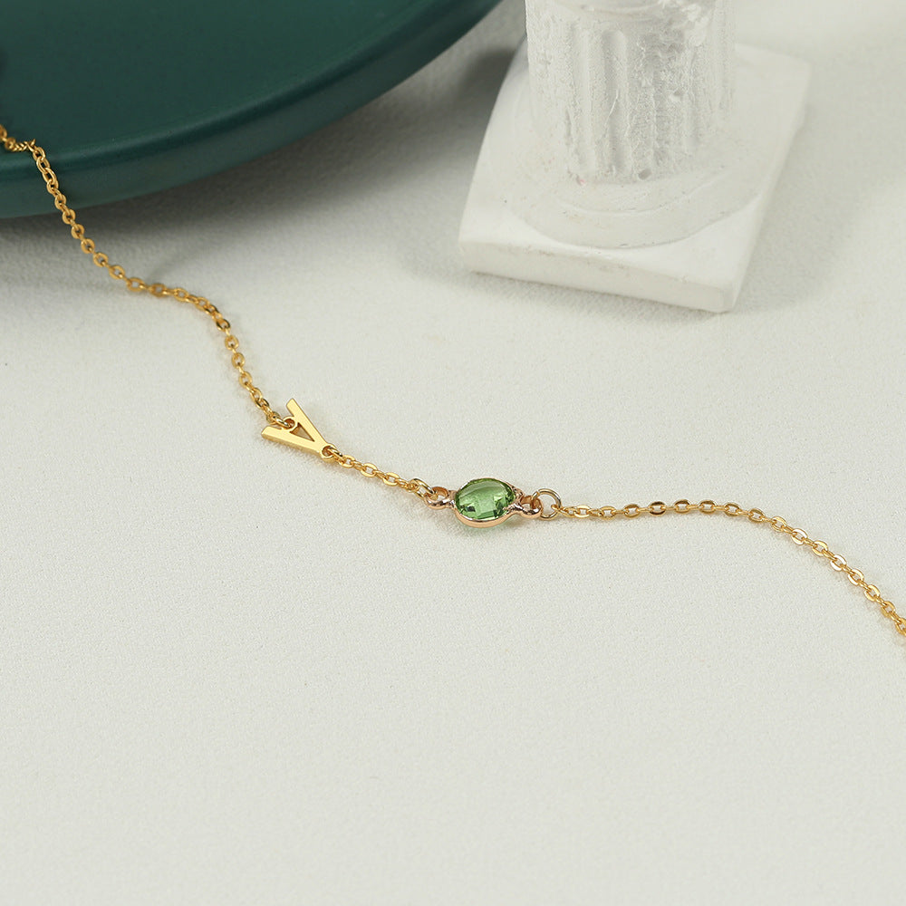 A gold-coloured bracelet with an emerald pendant and a customisable initial charm.