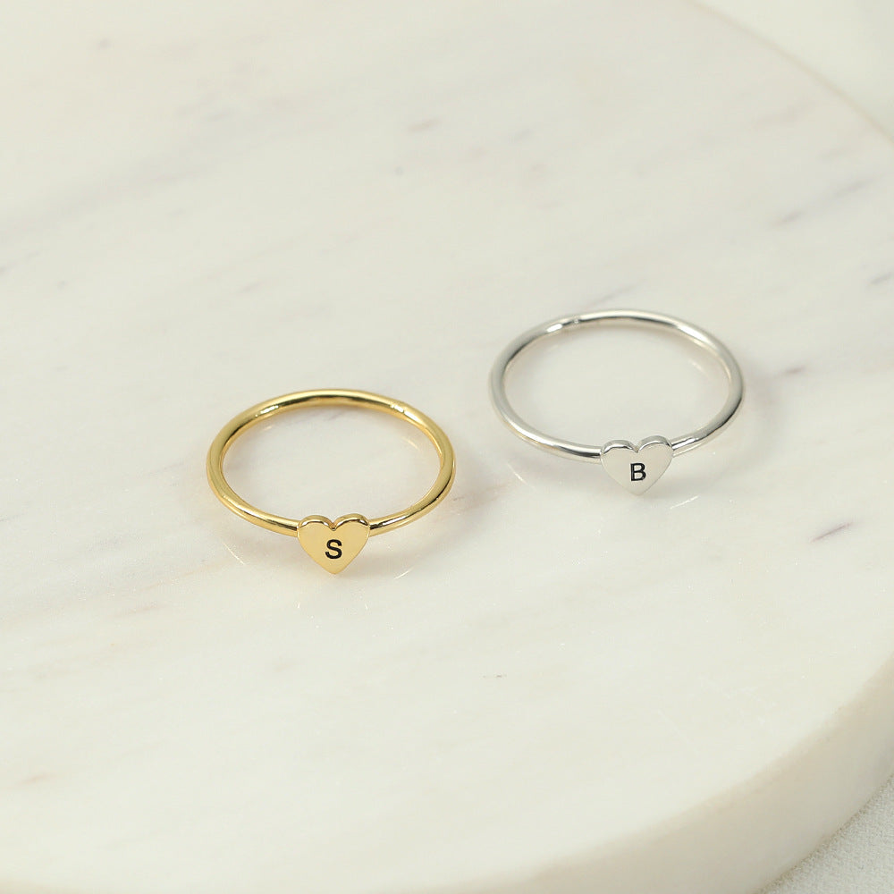 Two rings, one with a heart-shaped initial in gold colour and another in silver colour, placed on a marble surface.