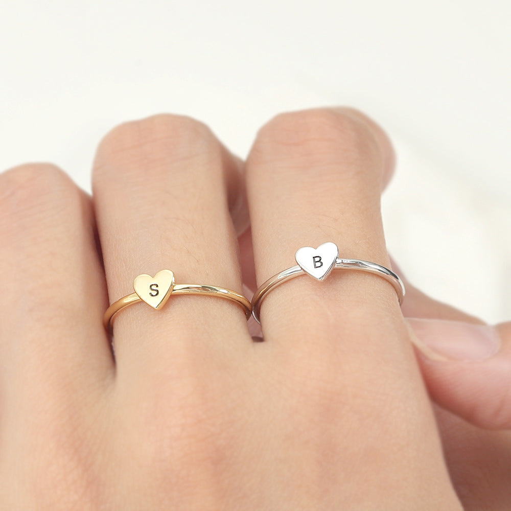 Two rings, one with a heart-shaped initial in gold colour and another in silver colour, on an index and middle finger.