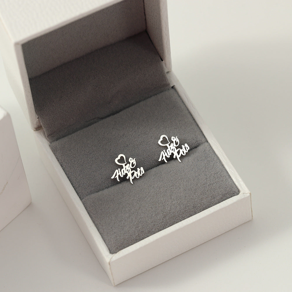 A pair of silver heart-shaped earrings with customisable name design displayed in a white and grey box.