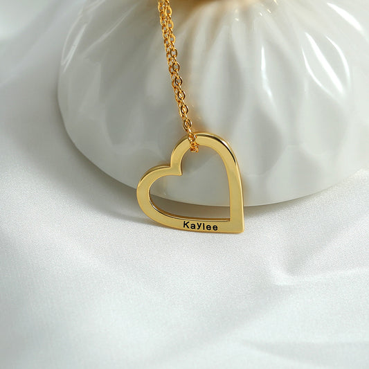 A necklace with a gold heart and customised with the name Kaylee, lying on a white surface.