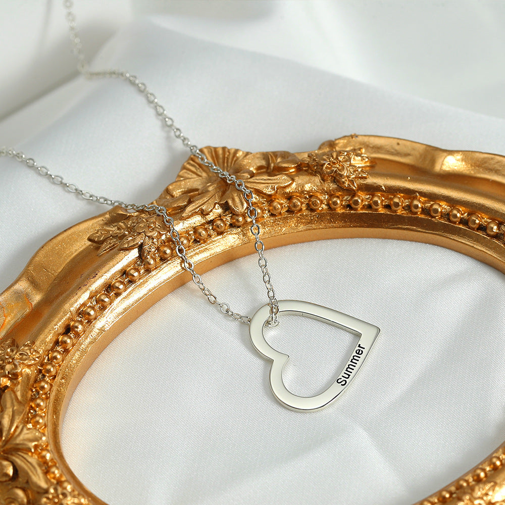 A necklace with a silver heart and customised with the name Summer, lying on a white surface and gold ornament.
