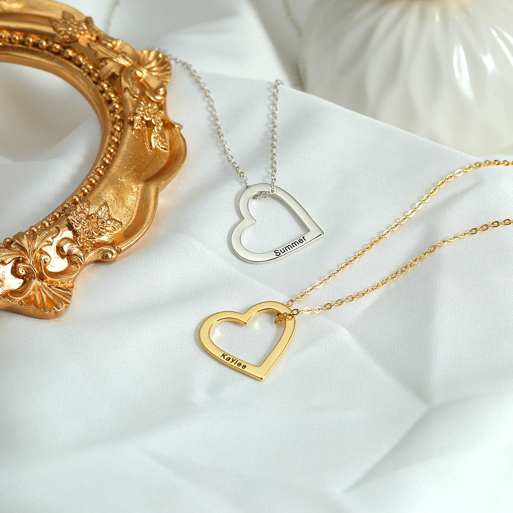 Two necklaces, one with a gold heart and the other with a silver heart, each customised with different names, lying on a white surface with a golden ornament in the background.