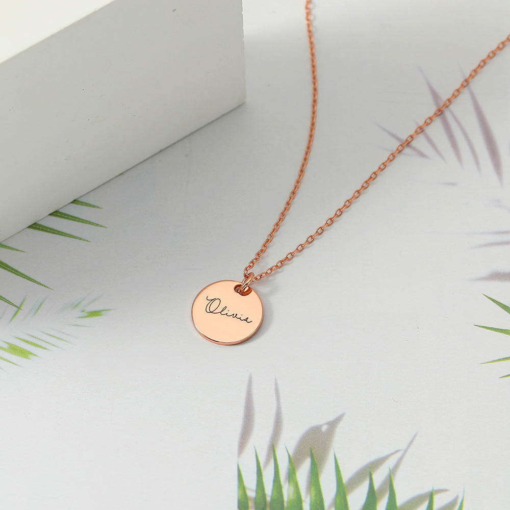 Rose gold disc necklace pendant displayed on a white background with palm leaves in the background.