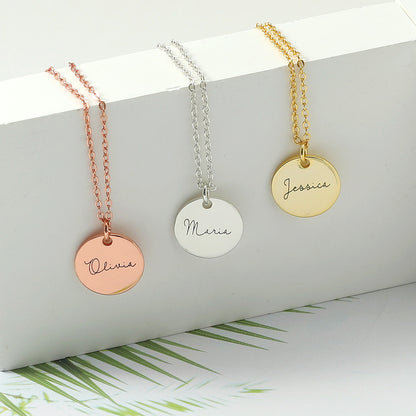 Three disc necklace pendants in rose gold, silver, and gold colours, displayed on a white background with palm leaves in the background.