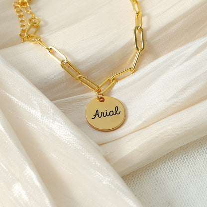 A gold-coloured bracelet with a round disc charm personalised with the name 'Arial'.