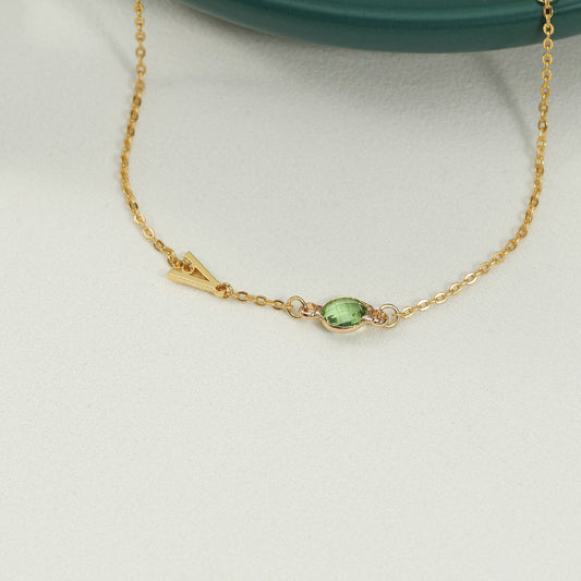 A gold-coloured bracelet with an emerald pendant and a customisable initial charm.