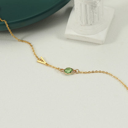 A gold-coloured bracelet with an emerald pendant and a customisable initial charm.