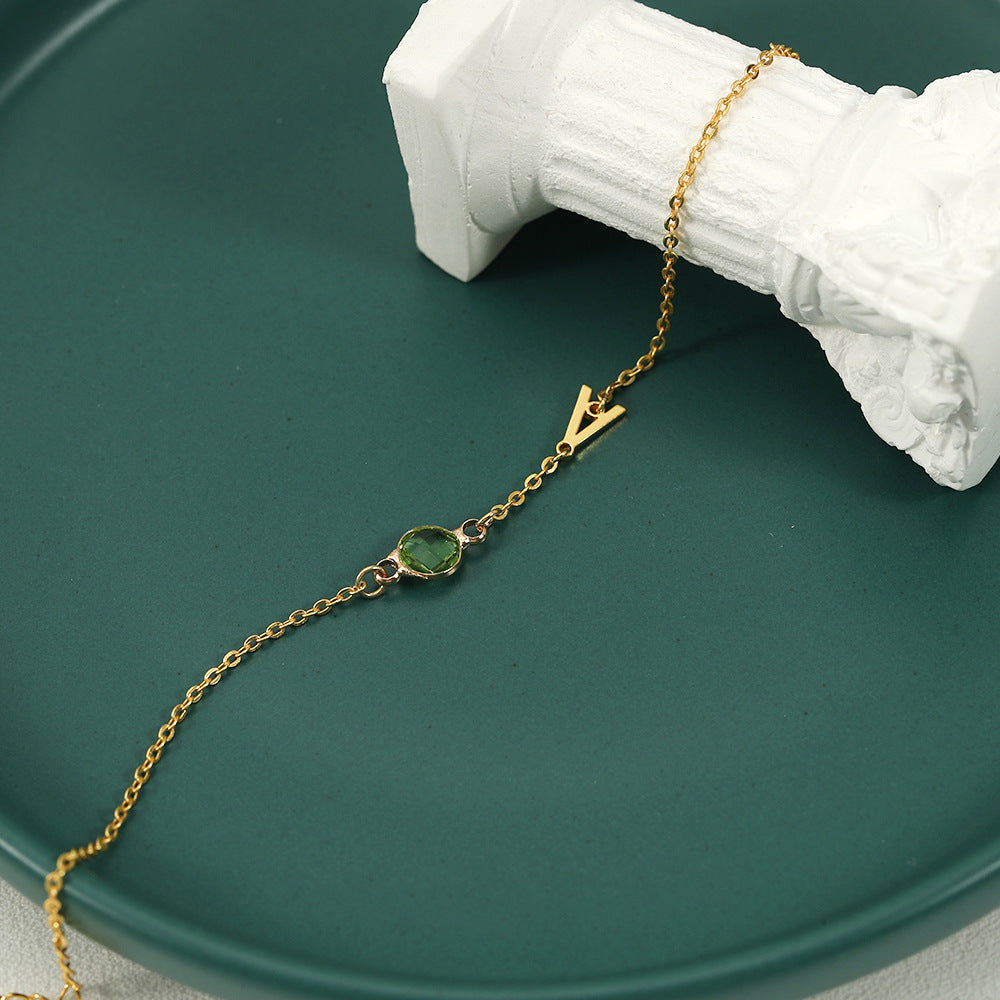 A gold-coloured bracelet with an emerald pendant and a customisable initial charm.