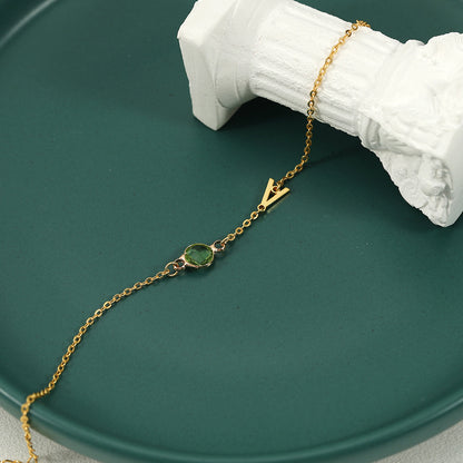 A gold-coloured bracelet with an emerald pendant and a customisable initial charm.