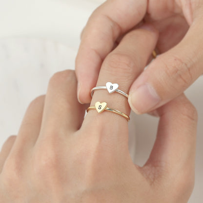 Two rings, one with a heart-shaped initial in gold color and another in silver color, on an index finger.