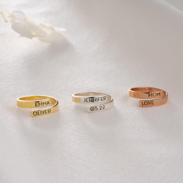 A gold, silver and rose gold ring with engraved names on a white surface