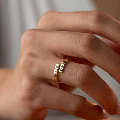 Close-up of a hand wearing gold wrap ring with engraved text on a neutral background