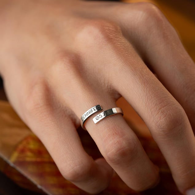 Close-up of a hand wearing a silver wrap ring with engraved text 