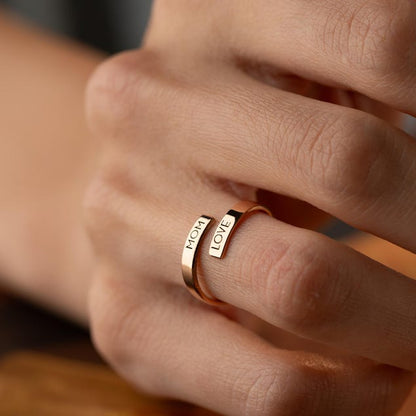 Close-up of a hand wearing a gold wrap ring with engraved text.