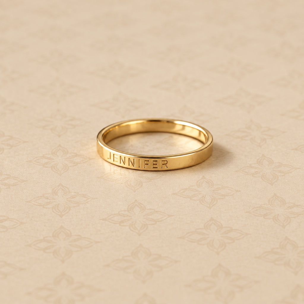 Gold ring with engraved name on a beige patterned surface
