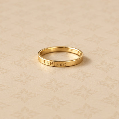 Gold ring with engraved name on a beige patterned surface