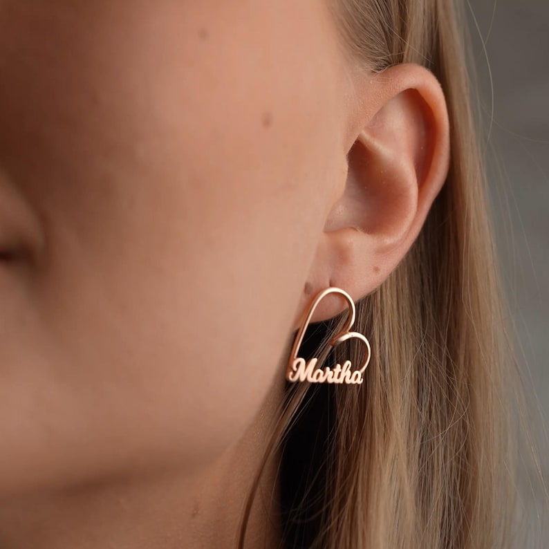 Gold hoop earrings with 'Martha' engraving worn by a person.