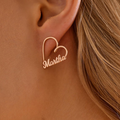 Rose gold heart-shaped earring with 'Martha' engraving worn by a person.