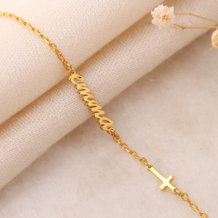 Gold bracelet with a cross charm on a beige fabric background