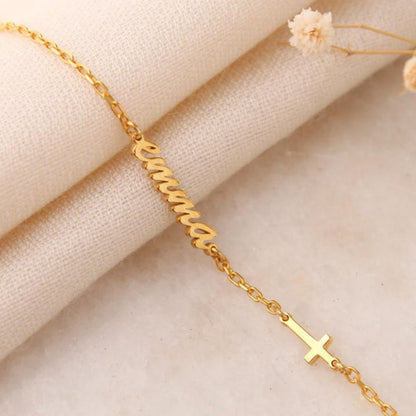 Gold bracelet with a cross charm on a beige fabric background