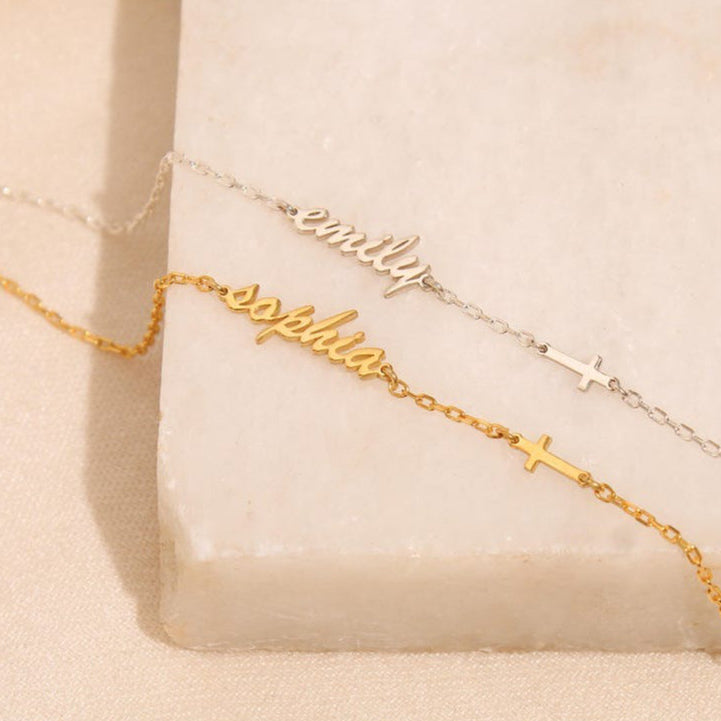 A gold and a silver name bracelet on a beige surface