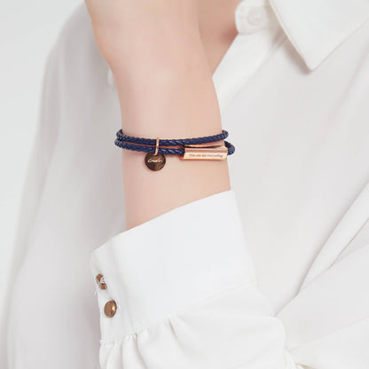 A black leather wrap bracelet with a stainless steel tag, with the tag displaying an engraving.