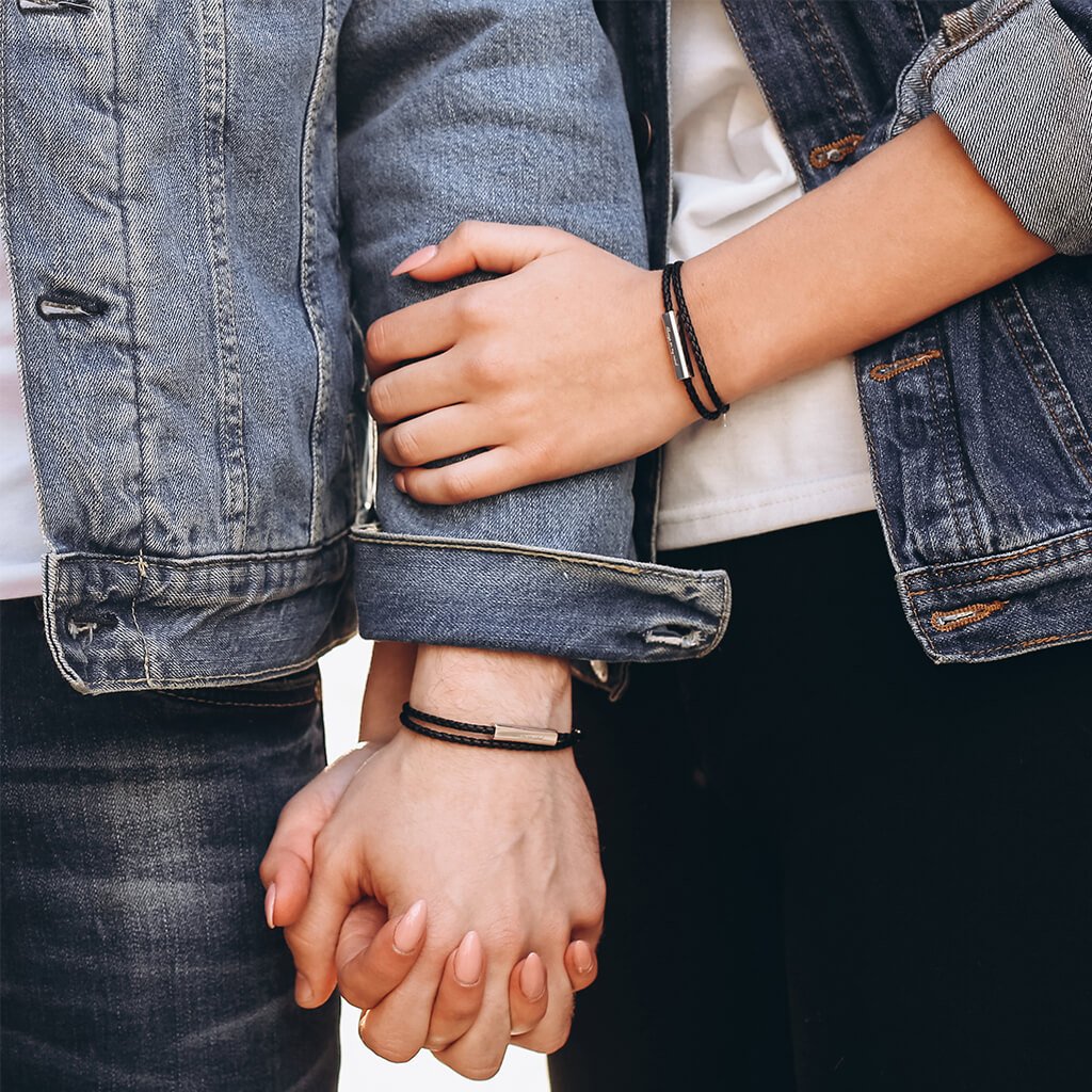 People wearing black leather wrap bracelets with a stainless steel tag, with the tag displaying an engraving.
