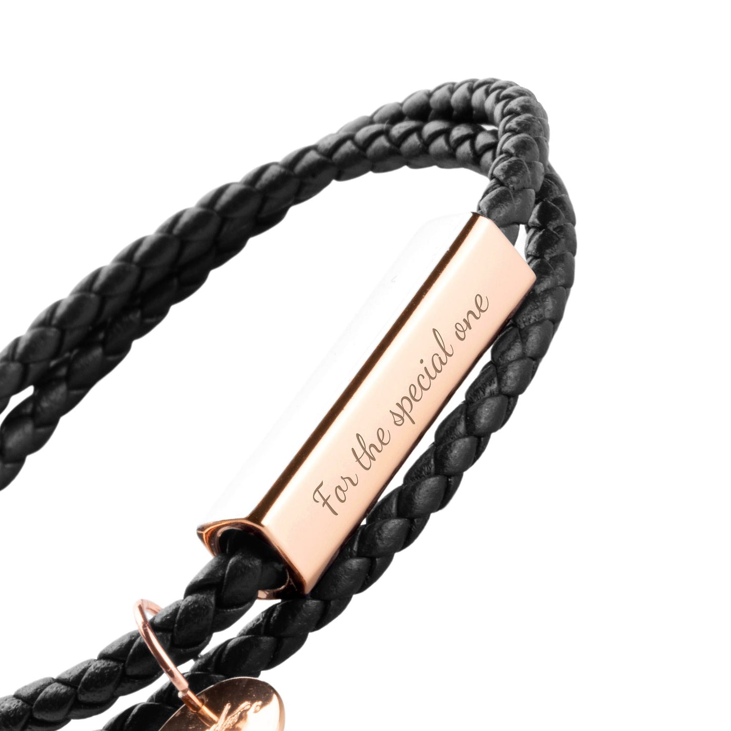 A black leather wrap bracelet with a stainless steel tag lying on an open book, with the tag displaying an engraving.