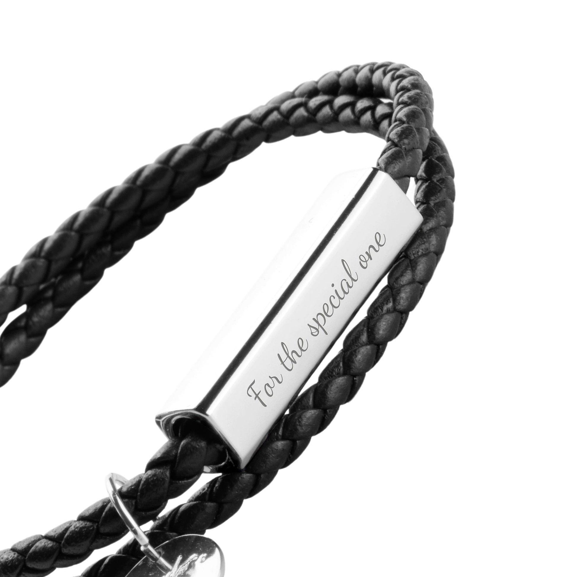 A black leather wrap bracelet with a stainless steel tag lying on an open book, with the tag displaying an engraving.