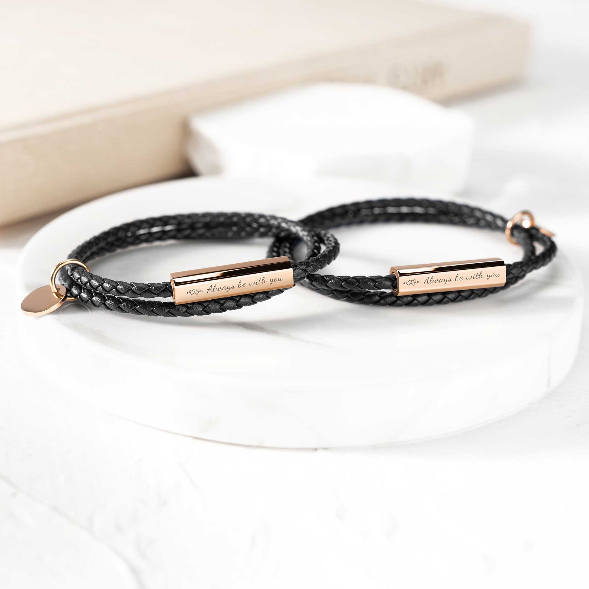 A black leather wrap bracelet with a stainless steel tag lying on an open book, with the tag displaying an engraving.
