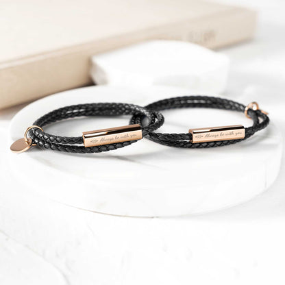 A black leather wrap bracelet with a stainless steel tag lying on an open book, with the tag displaying an engraving.