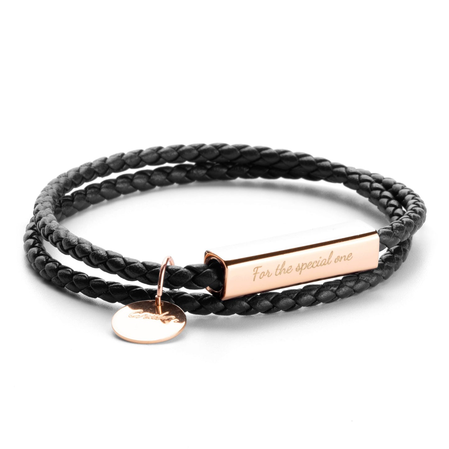 A black leather wrap bracelet with a stainless steel tag lying on an open book, with the tag displaying an engraving.