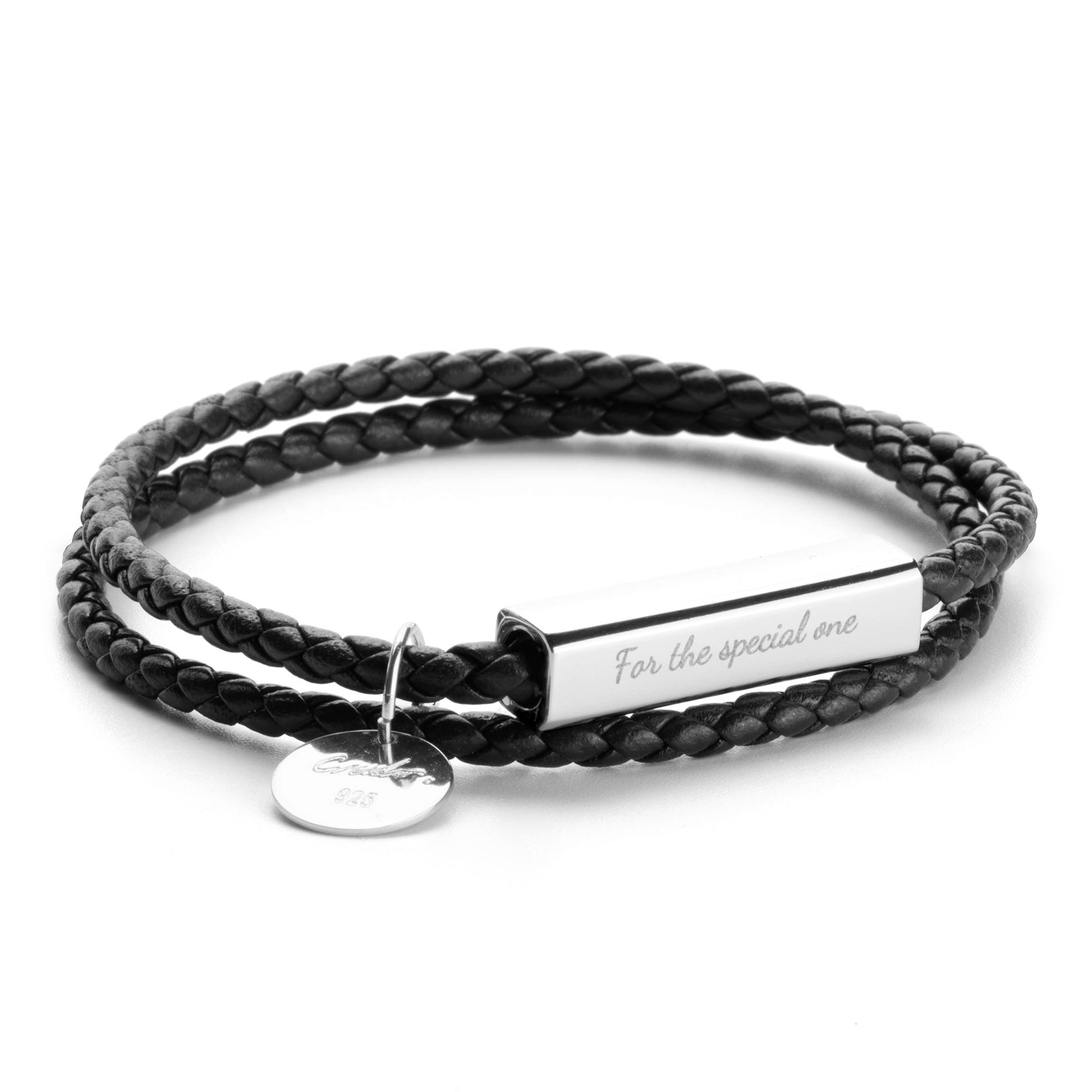 A black leather wrap bracelet with a stainless steel tag lying on an open book, with the tag displaying an engraving.