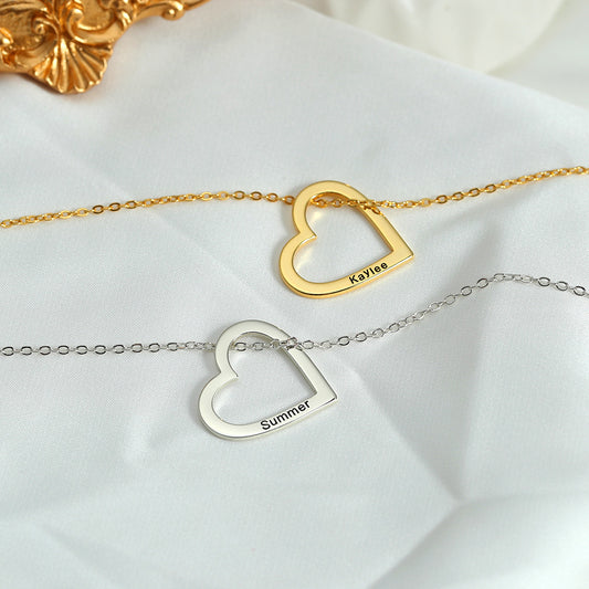 Two necklaces, one with a gold heart and the other with a silver heart, each customised with different names, lying on a white surface with a golden ornament in the background.
