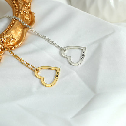 Two necklaces, one with a gold heart and the other with a silver heart, each customised with different names, lying on a white surface with a golden ornament in the background.
