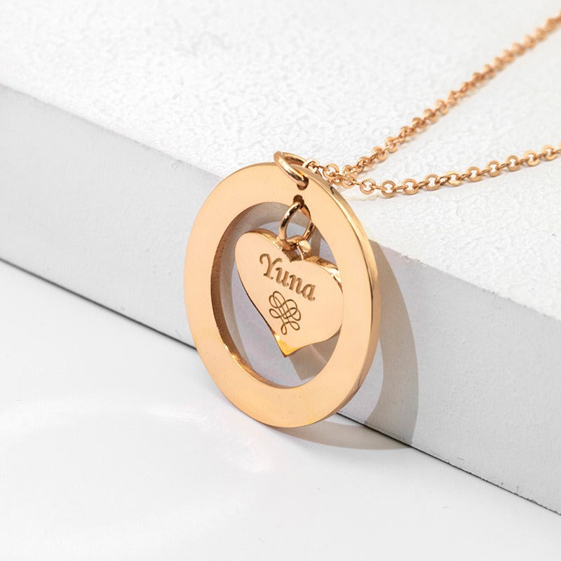 A rose gold necklace with a hollow round pendant containing a suspended love heart and a customisable name design, displayed against a white background.