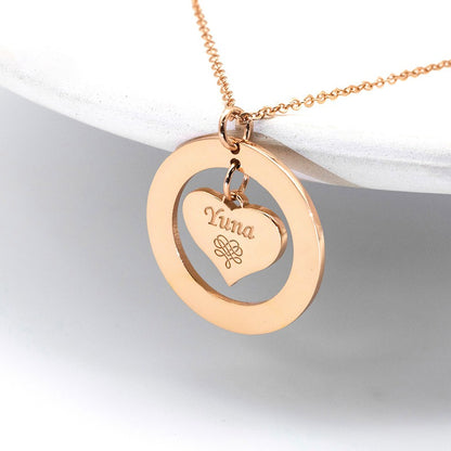A rose gold necklace with a hollow round pendant containing a suspended love heart and a customisable name design, displayed against a white background.