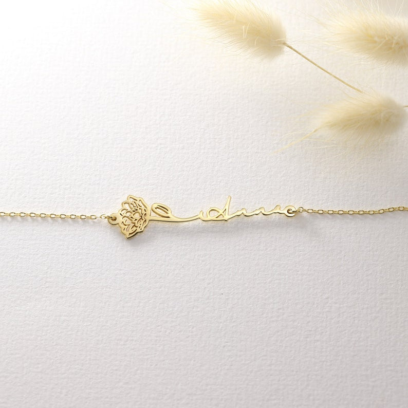 Gold bracelet with a name and flower on a light background