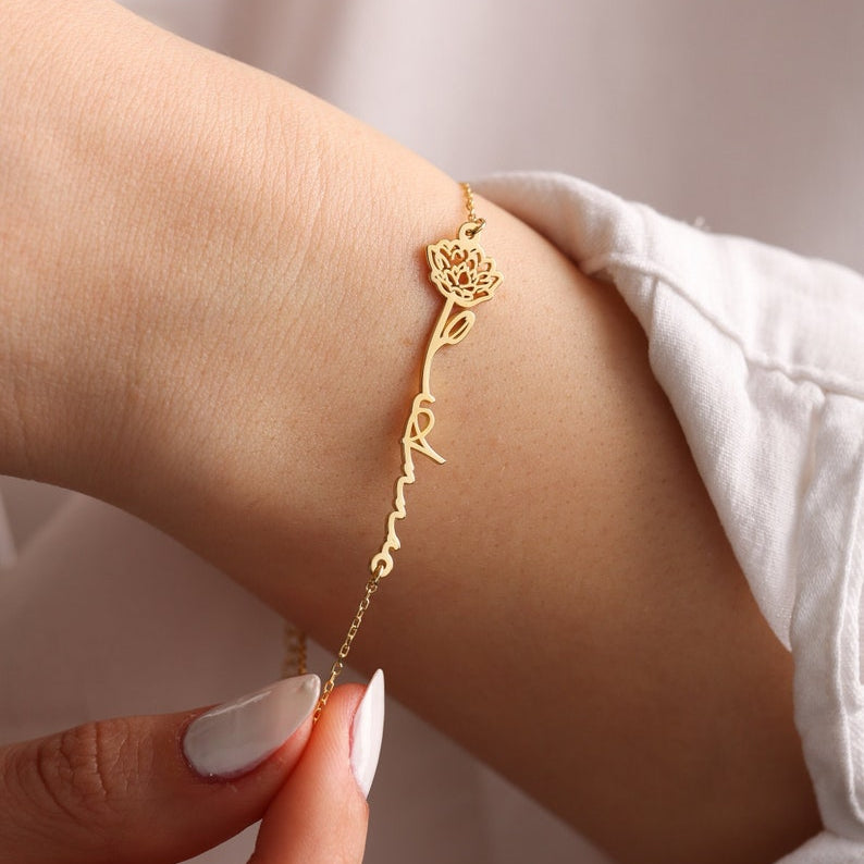 Gold bracelet with a name and flower on a wrist with a plain background