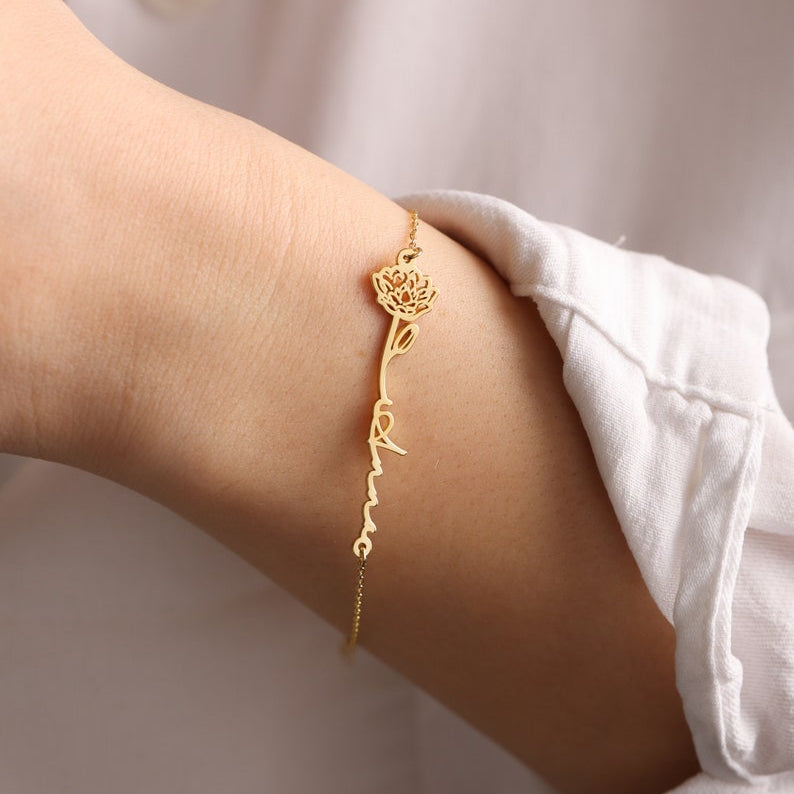 Gold bracelet with a name and flower on a wrist with a blurred background