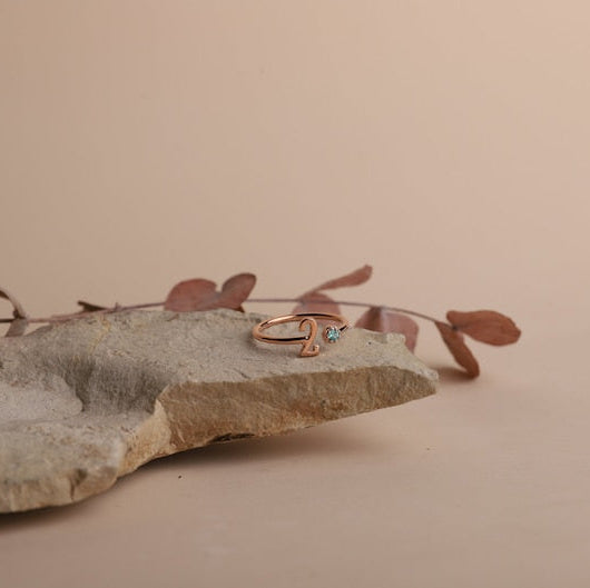 Rose gold ring with a blue gemstone on a stone surface with dried leaves.