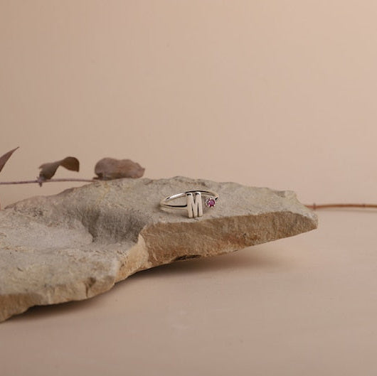Silver ring with a red gemstone on a textured stone surface against a beige background